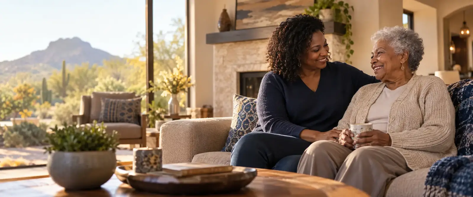 A caregiver sitting with an older woman in a bright, comfortable living room
