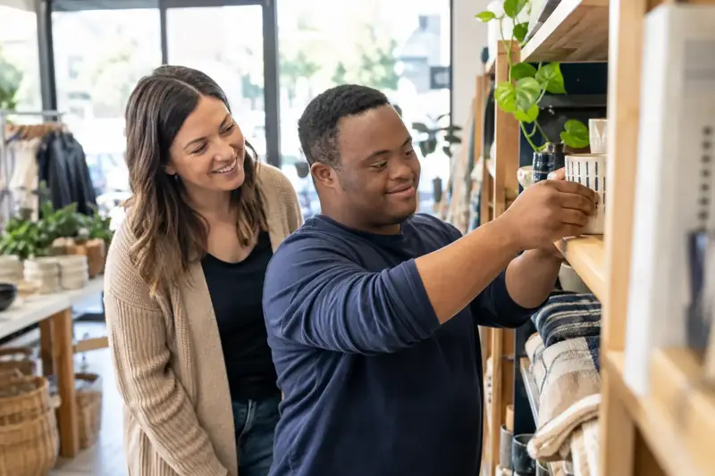 A support worker helping a young man choose items in a store